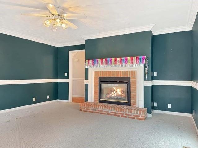 unfurnished living room featuring ceiling fan, crown molding, carpet floors, and a brick fireplace