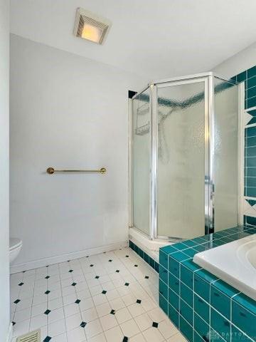 bathroom with tile patterned floors, a shower with shower door, and toilet