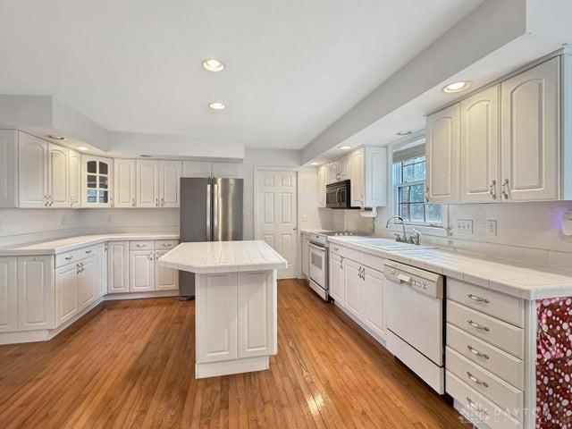 kitchen featuring light wood-type flooring, white appliances, tile countertops, a center island, and white cabinetry