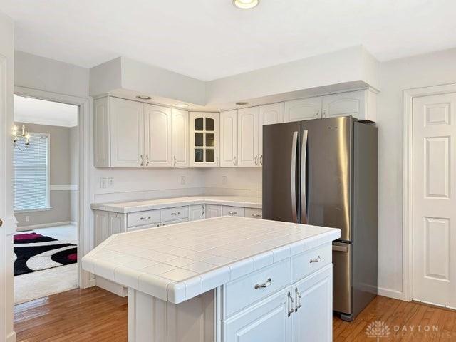 kitchen featuring stainless steel fridge, tile countertops, white cabinets, hardwood / wood-style floors, and a kitchen island