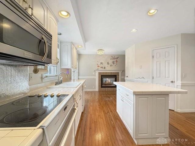 kitchen with white cabinets, sink, light hardwood / wood-style flooring, tile counters, and range