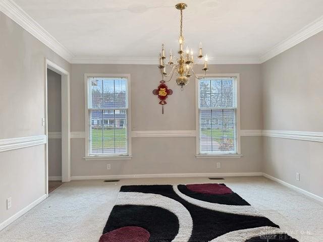 carpeted dining space with a healthy amount of sunlight, ornamental molding, and a chandelier