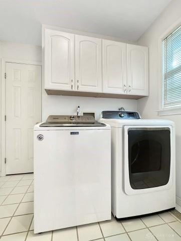 laundry area with washing machine and clothes dryer, light tile patterned floors, and cabinets