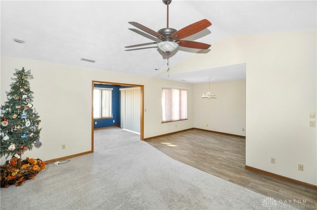 spare room featuring ceiling fan with notable chandelier, light wood-type flooring, and vaulted ceiling