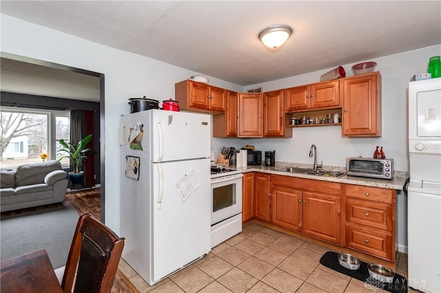 kitchen featuring sink, light tile patterned floors, stacked washing maching and dryer, and white appliances