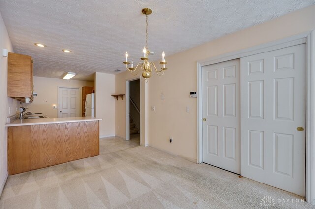 kitchen featuring white refrigerator, sink, an inviting chandelier, kitchen peninsula, and pendant lighting