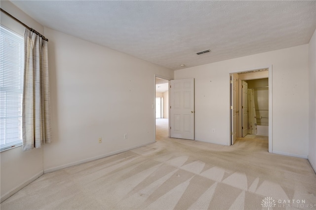 unfurnished bedroom with connected bathroom, a textured ceiling, and light carpet