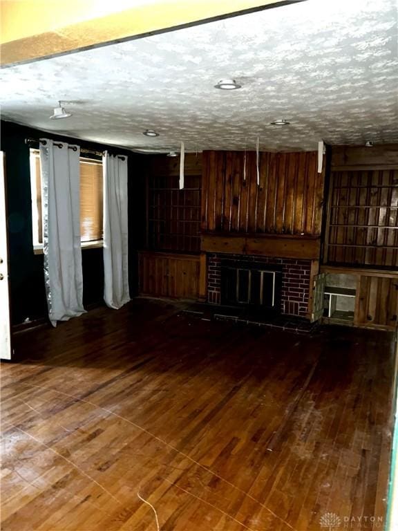 unfurnished living room featuring hardwood / wood-style floors, a textured ceiling, and a brick fireplace