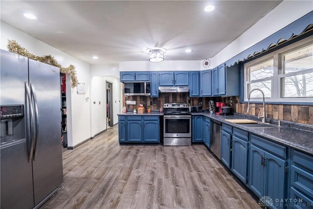 kitchen featuring sink, stainless steel appliances, tasteful backsplash, blue cabinets, and light wood-type flooring