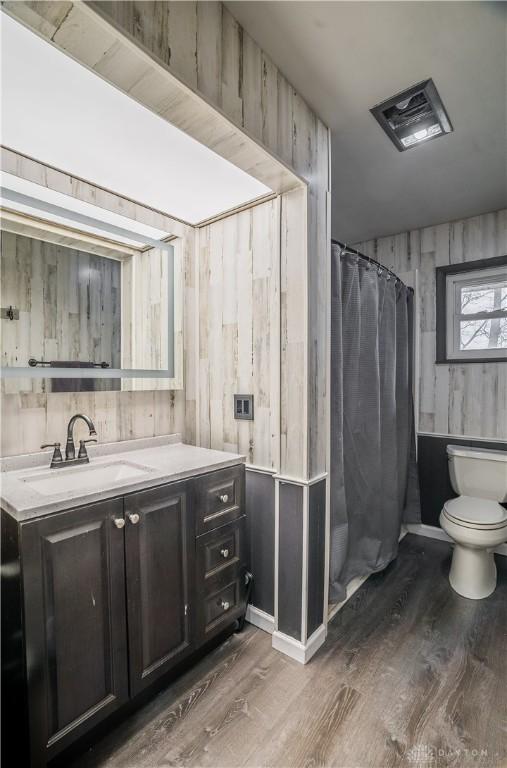 bathroom with vanity, hardwood / wood-style flooring, toilet, and wood walls