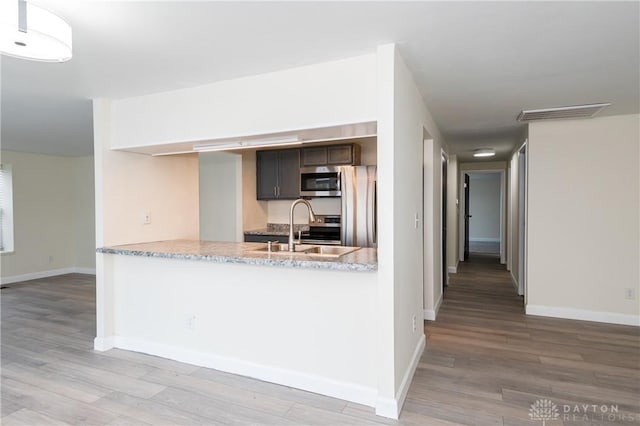 kitchen with kitchen peninsula, light wood-type flooring, dark brown cabinets, stainless steel appliances, and sink