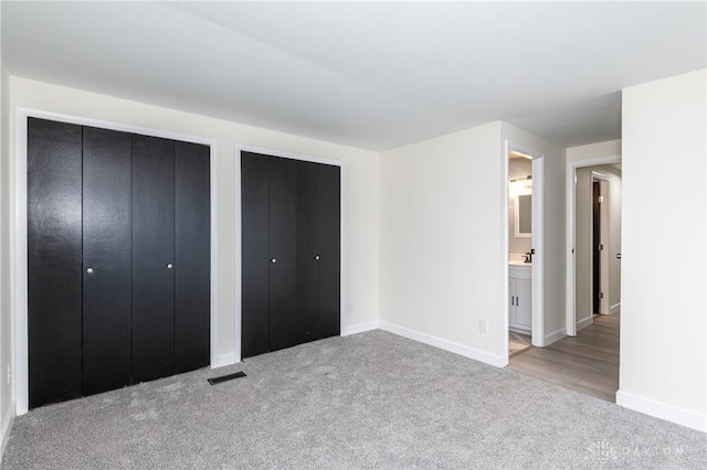 unfurnished bedroom featuring multiple closets, light carpet, and ensuite bath