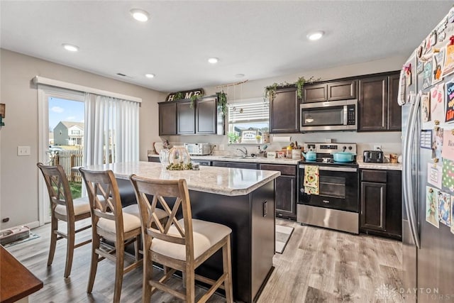 kitchen featuring light wood-type flooring, stainless steel appliances, a kitchen island, and dark brown cabinetry