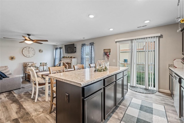 kitchen featuring ceiling fan, light stone countertops, light wood-type flooring, a kitchen island, and a breakfast bar area