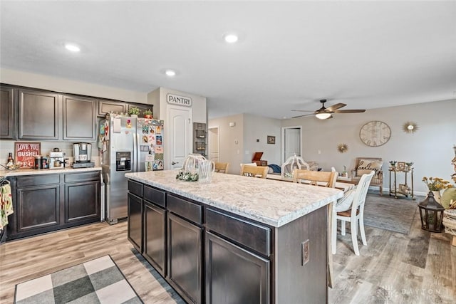 kitchen featuring a center island, ceiling fan, stainless steel fridge, light wood-type flooring, and dark brown cabinets