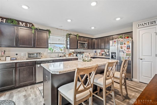 kitchen with appliances with stainless steel finishes, light wood-type flooring, dark brown cabinets, a kitchen island, and a breakfast bar area