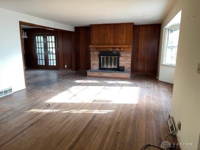 unfurnished living room with wood walls, wood-type flooring, french doors, and a brick fireplace