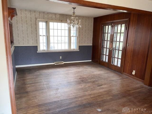 unfurnished dining area featuring a notable chandelier, dark wood-type flooring, and french doors