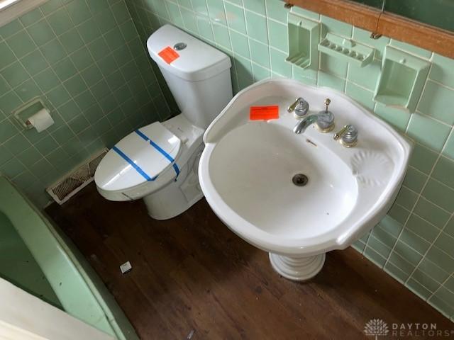 bathroom featuring tasteful backsplash, hardwood / wood-style floors, tile walls, and toilet