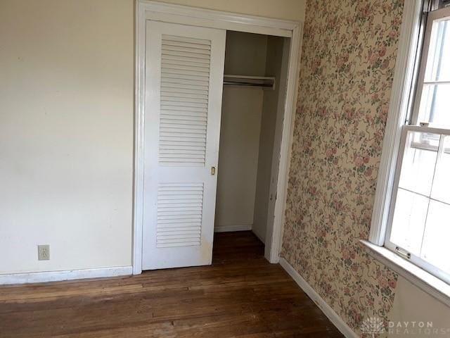 unfurnished bedroom with multiple windows, a closet, and dark wood-type flooring