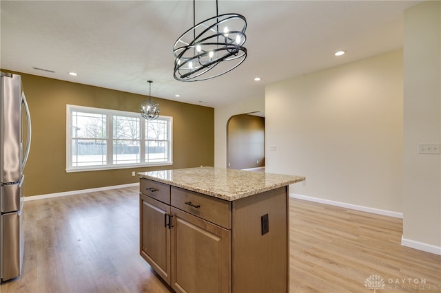 kitchen featuring stainless steel refrigerator, hanging light fixtures, light stone counters, a kitchen island, and light wood-type flooring