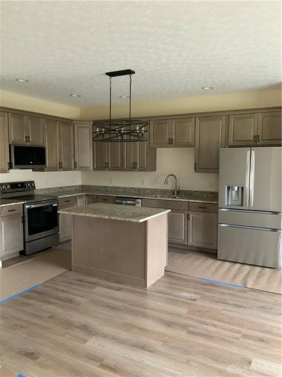 kitchen featuring a center island, sink, light wood-type flooring, appliances with stainless steel finishes, and decorative light fixtures