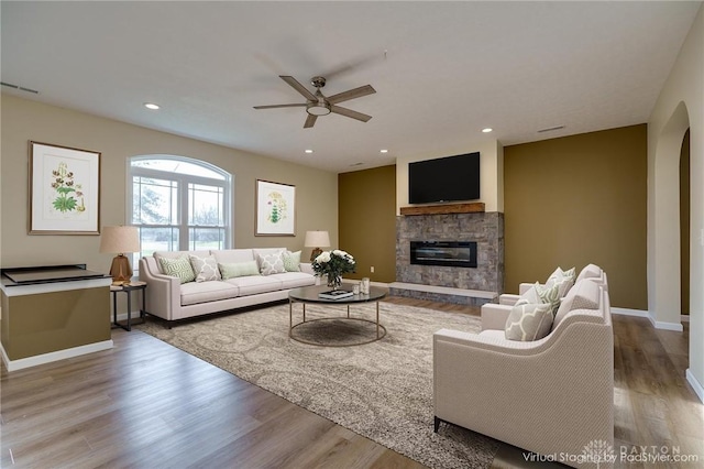 living room with light hardwood / wood-style flooring, ceiling fan, and a stone fireplace