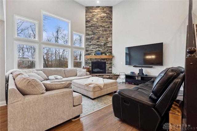 living room featuring hardwood / wood-style flooring, a stone fireplace, and a high ceiling