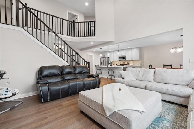 living room featuring a towering ceiling, wood-type flooring, and a notable chandelier