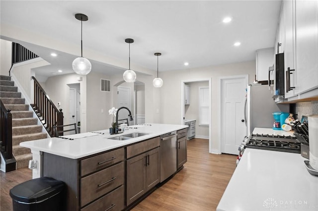 kitchen with sink, stainless steel dishwasher, an island with sink, decorative light fixtures, and dark brown cabinetry