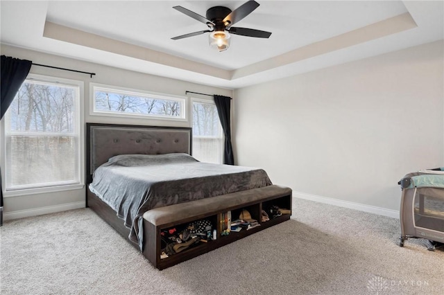 carpeted bedroom with a raised ceiling and ceiling fan