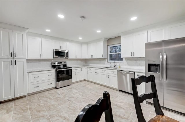 kitchen with white cabinetry, sink, light stone countertops, decorative backsplash, and appliances with stainless steel finishes