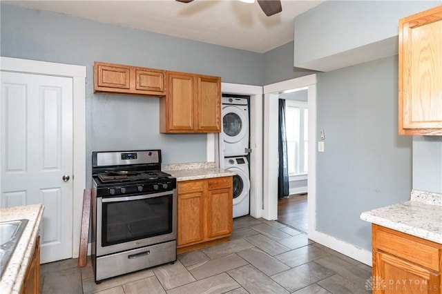 kitchen featuring light stone countertops, stainless steel gas range oven, ceiling fan, sink, and stacked washer / dryer