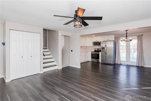 unfurnished living room with ceiling fan with notable chandelier and dark wood-type flooring