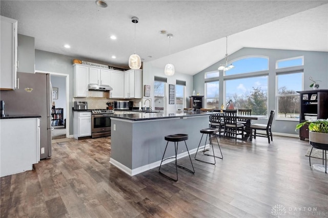 kitchen with a kitchen bar, appliances with stainless steel finishes, tasteful backsplash, pendant lighting, and white cabinets