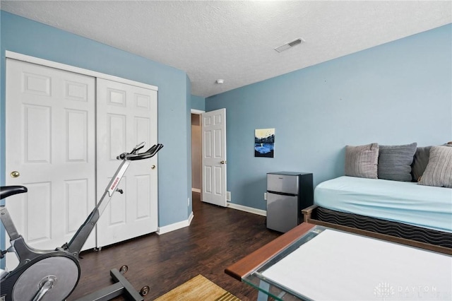 bedroom with a textured ceiling, dark hardwood / wood-style floors, stainless steel refrigerator, and a closet