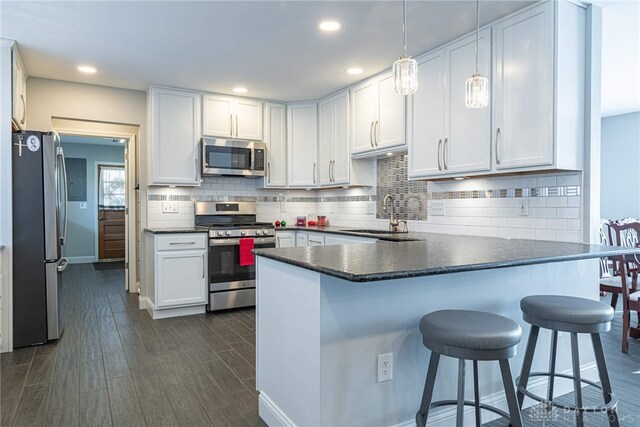 kitchen featuring dark wood finished floors, stainless steel appliances, dark countertops, a sink, and a peninsula