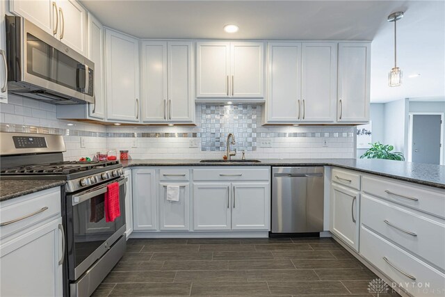 kitchen with tasteful backsplash, dark stone counters, stainless steel appliances, white cabinetry, and a sink