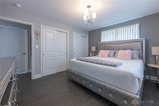 bedroom with baseboards, a chandelier, dark wood-style flooring, and two closets