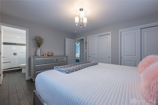 bedroom with a chandelier, ensuite bath, dark wood finished floors, and multiple closets