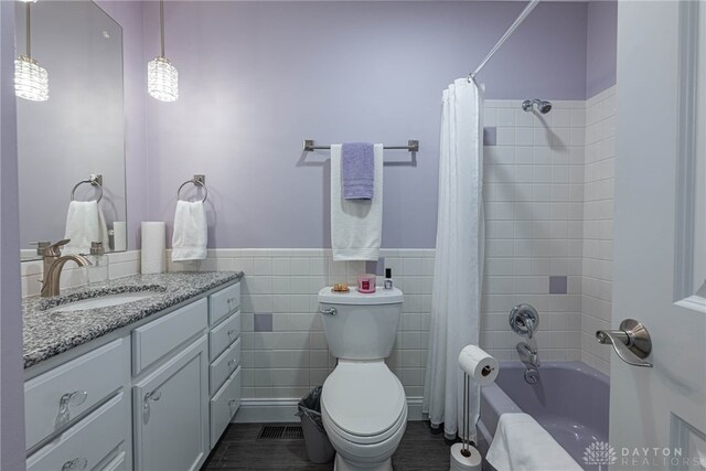 full bath with toilet, a wainscoted wall, tile walls, vanity, and shower / bathtub combination with curtain