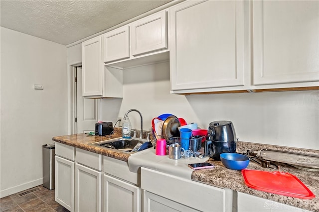 kitchen featuring a textured ceiling, white cabinetry, and sink