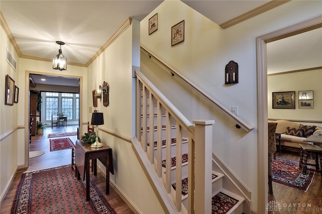 staircase featuring hardwood / wood-style flooring, ornamental molding, and a chandelier