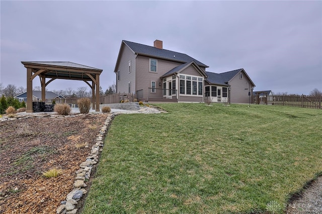 rear view of property featuring a gazebo, a sunroom, a patio, and a lawn