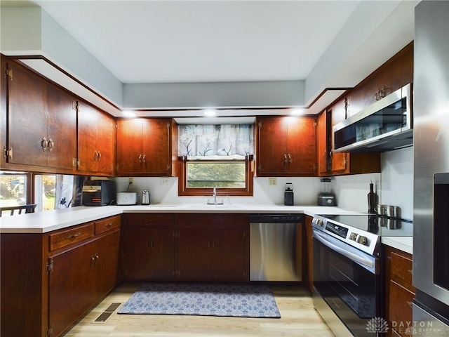 kitchen featuring kitchen peninsula, appliances with stainless steel finishes, decorative backsplash, sink, and light hardwood / wood-style floors