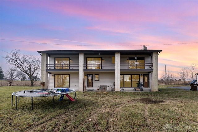 back house at dusk featuring a lawn, a balcony, and a trampoline