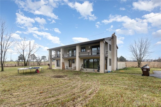 back of property with a trampoline, a balcony, and a lawn