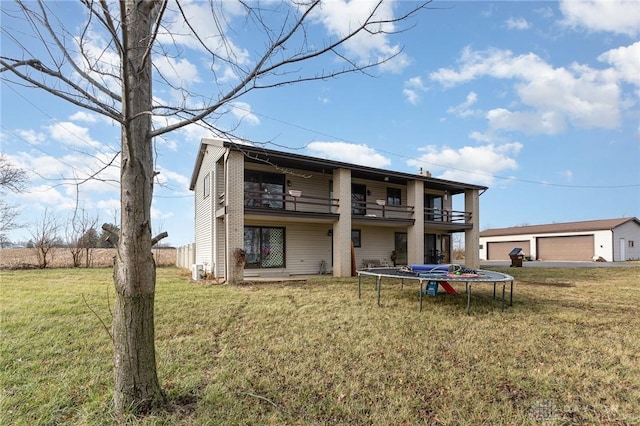 back of house featuring a balcony, an outdoor structure, a yard, a trampoline, and a garage