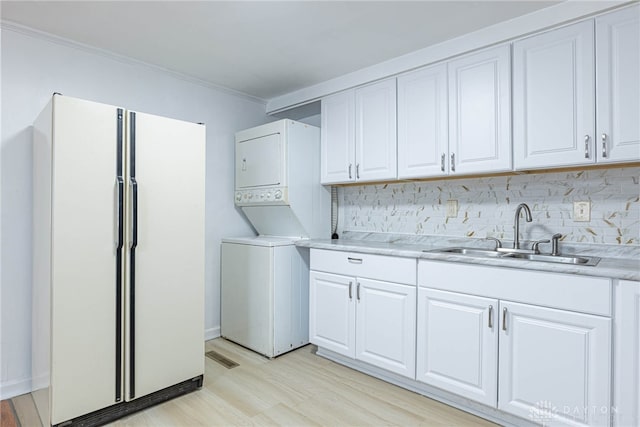 laundry room featuring stacked washer / drying machine, crown molding, light wood-type flooring, and sink