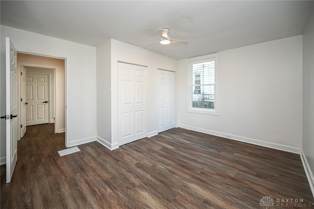 unfurnished bedroom with ceiling fan, dark hardwood / wood-style floors, and multiple closets